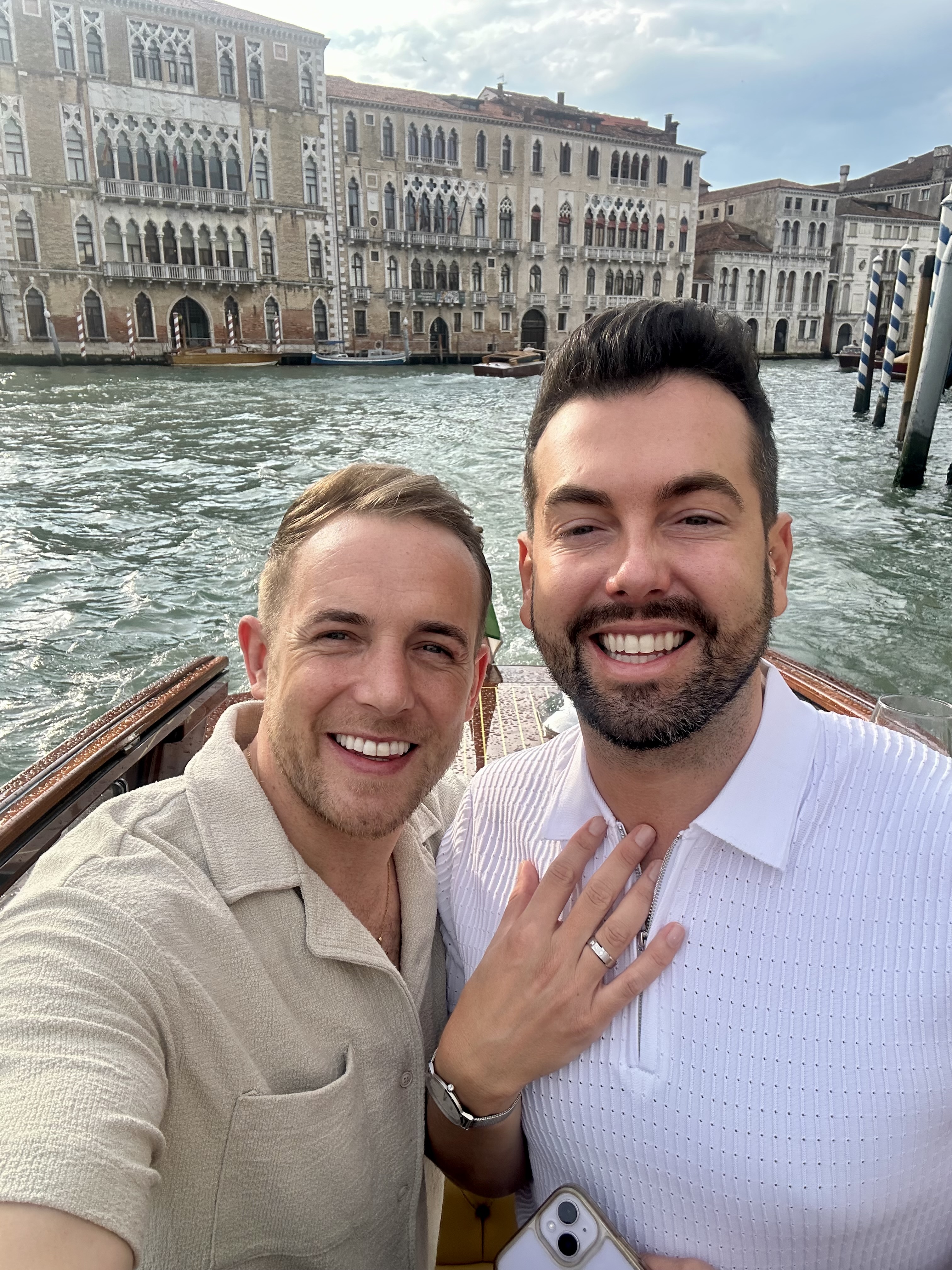 Mark and Mikey beaming on a boat in Venice, showing off the engagement ring