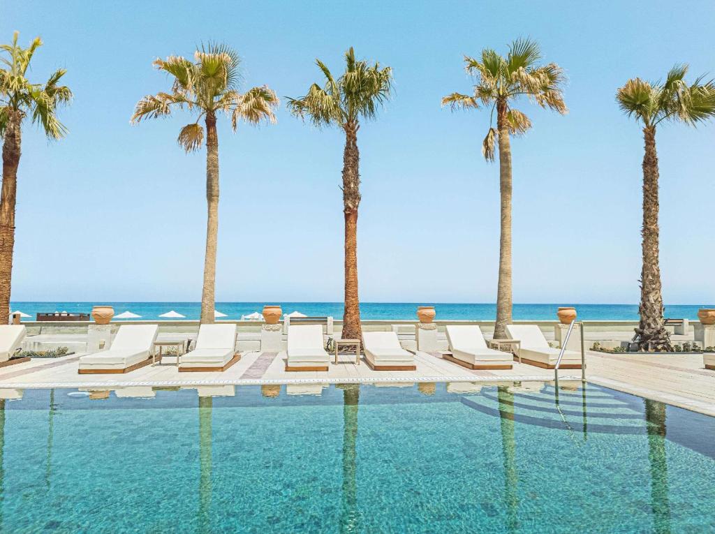 Beachfront pool with palm trees and sun loungers at Grecotel Plaza Beach House