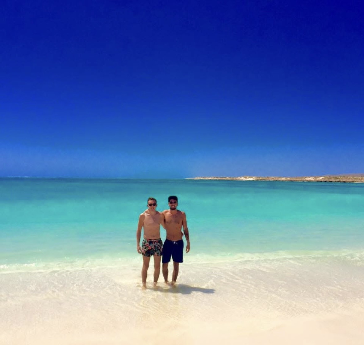 Mark and Mikey paddling in turquoise water on a white-sand beach